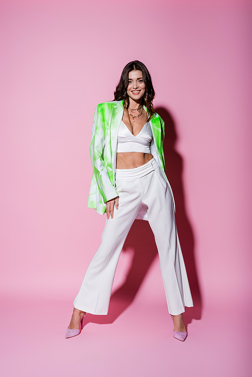 full length of smiling woman in stylish outfit posing on pink