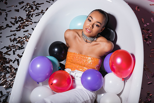 high angle view of african american woman lying in bathtub with colorful balloons