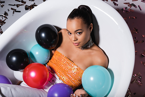 high angle view of young african american woman lying in bathtub with balloons