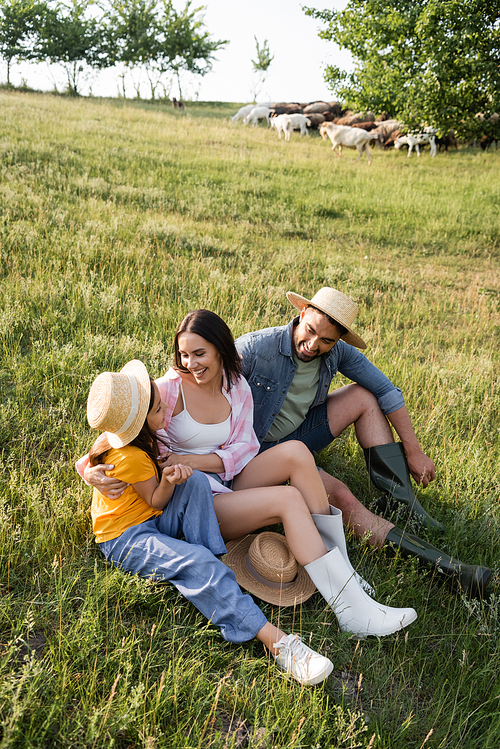 smiling farmers with daughter sitting in green meadow on summer day