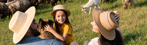 girl in straw hat smiling near cattle dog and parents on green pasture, banner