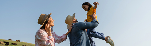 low angle view of farmer playing with daughter near happy wife under blue sky, banner