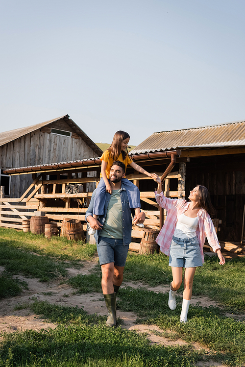 cheerful man piggybacking daughter while walking near wife on rural farm