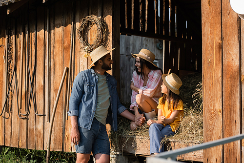 man in straw hat talking to wife and daughter sitting on hay in wooden barn