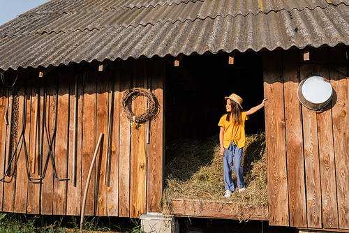 full length of girl standing on hey in wooden barn and looking away