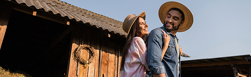 happy woman in straw hat embracing bearded husband near wooden barn, banner