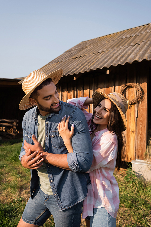 joyful woman in straw hat hugging husband on farm in countryside