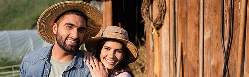 cheerful couple of farmers in straw hats smiling at camera on family farm, banner