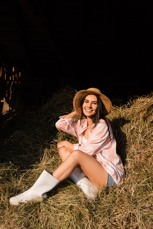 happy farm woman in straw hat sitting on haystack and looking at camera