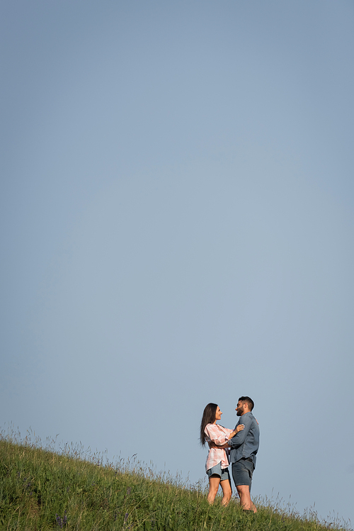 happy couple standing face to face and embracing on slope under blue sky