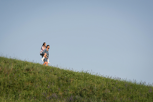 view from afar on man piggybacking girlfriend on grassy slope