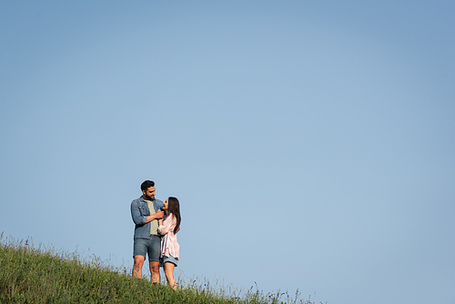 romantic couple looking at each other and embracing in field under blue sky