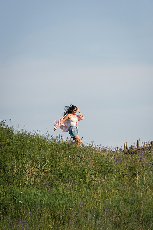 excited woman running in grassy field with wildflowers on summer day