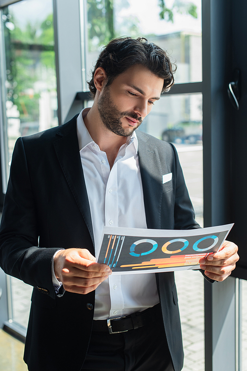 businessman in black blazer and white shirt looking at infographics in office