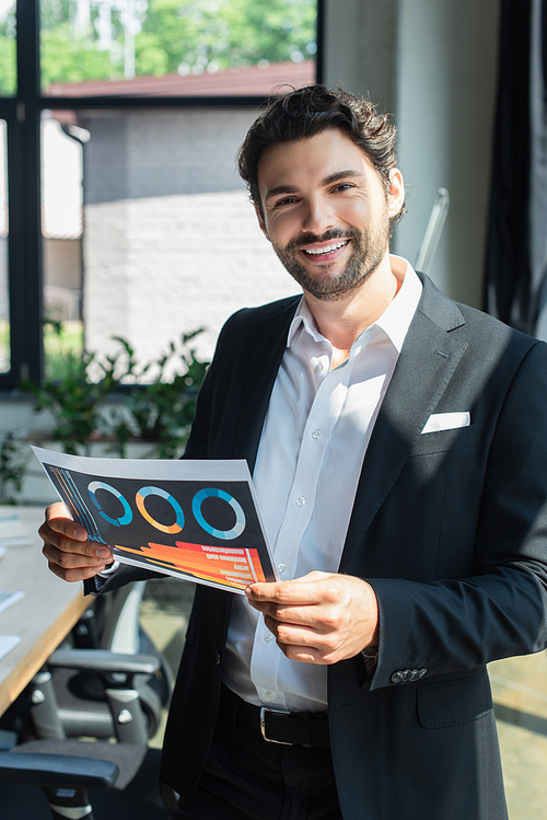 stylish businessman in black blazer and white shirt holding infographics in office