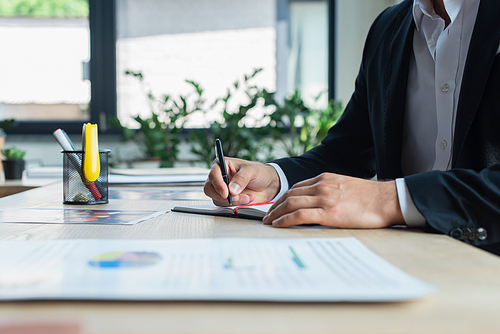 partial view of businessman writing in notebook while working in office