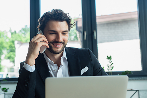 stylish and happy businessman talking on mobile phone in office