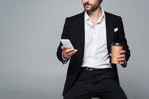 partial view of elegant man with takeaway drink and mobile phone sitting isolated on grey