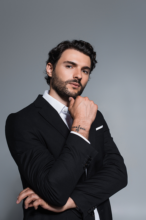 tattooed man in black blazer looking at camera isolated on grey