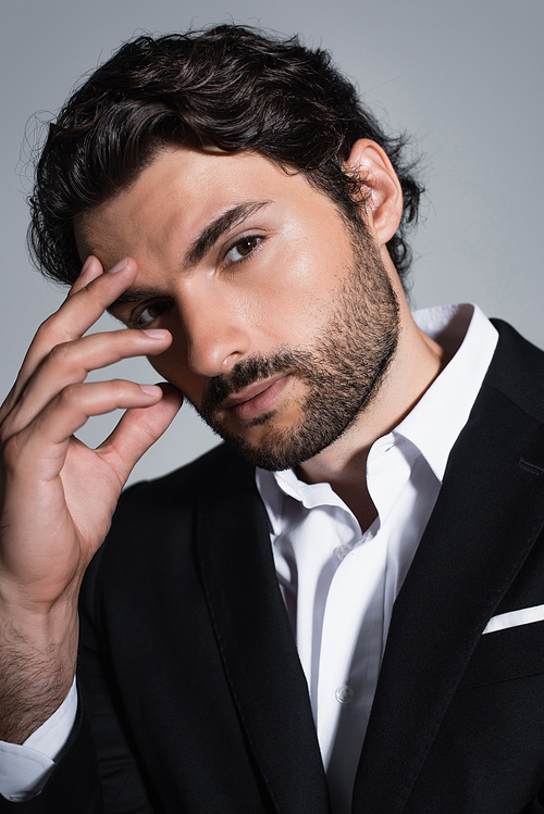 brunette bearded man holding hand near face and looking at camera isolated on grey