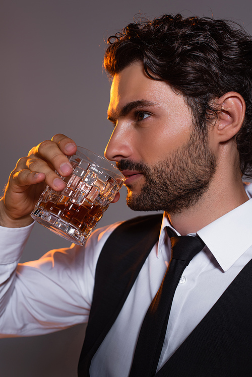 brunette man in white shirt and black tie drinking whiskey isolated on grey