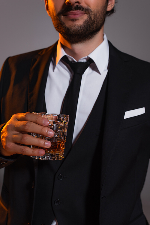 cropped view of man in elegant formal wear holding glass of whiskey isolated on grey