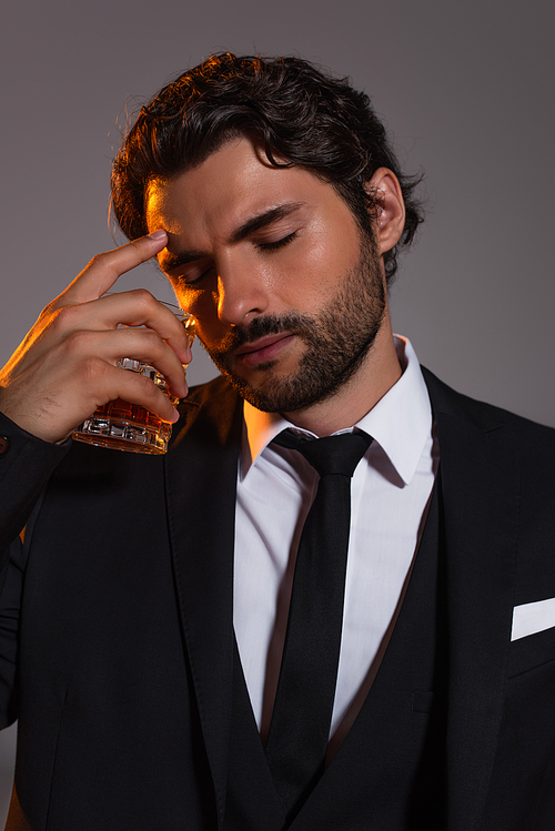 tired businessman with closed eyes holding glass of whiskey isolated on grey