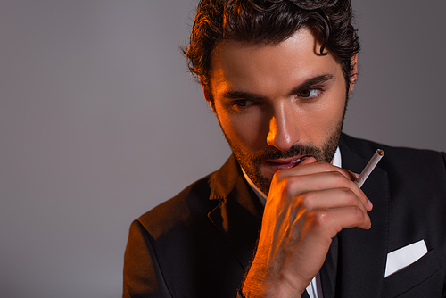 thoughtful man in black blazer holding cigarette isolated on grey