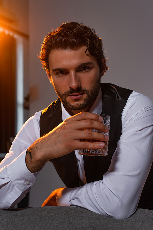 elegant businessman with glass of whiskey looking at camera on grey background