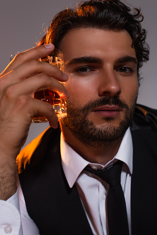 close up view of brunette man with glass of whiskey looking at camera isolated on grey