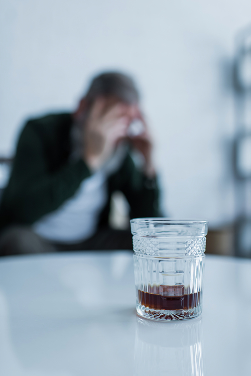 glass of whiskey on white coffee table near blurred man suffering crisis