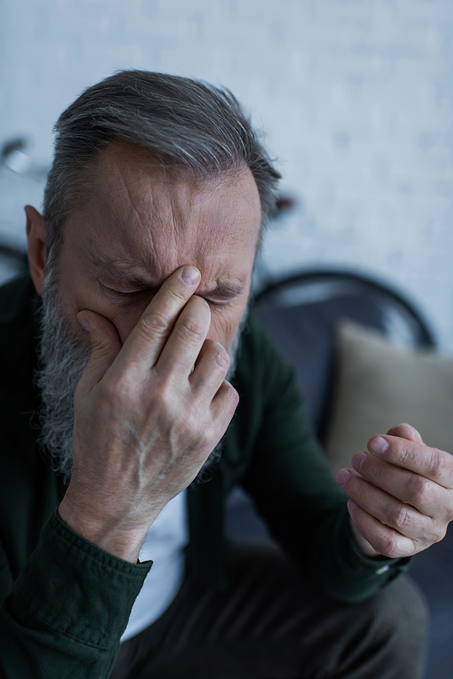 senior man with beard covering face while suffering from headache