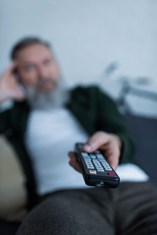 blurred senior man holding remote controller while watching tv