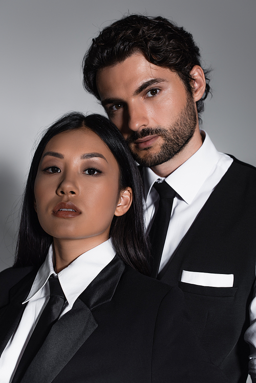 brunette asian woman and stylish bearded man looking at camera on grey background