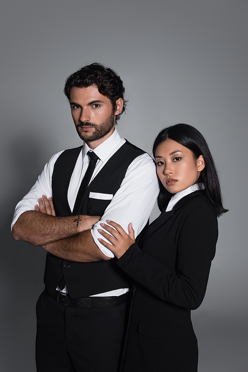 stylish man standing with crossed arms near young asian woman on grey background