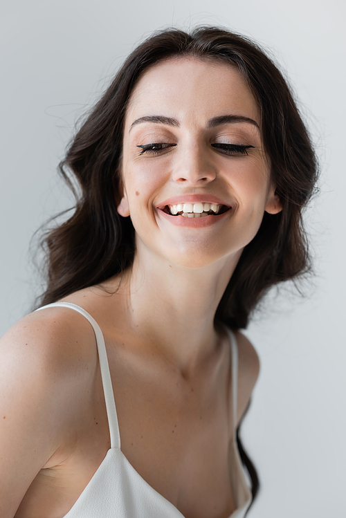 Smiling woman with makeup looking away isolated on grey