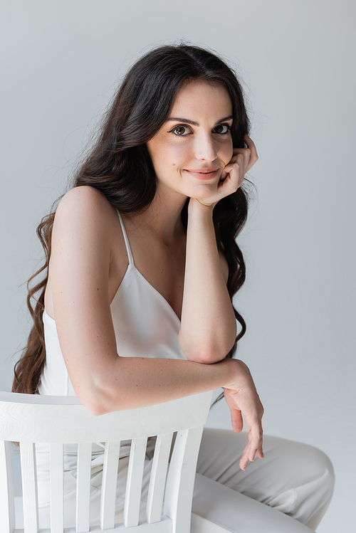 Portrait of pretty woman in white clothes sitting on chair isolated on grey