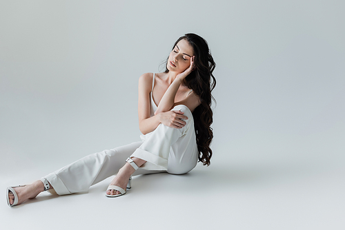 Stylish woman in white clothes sitting on grey background