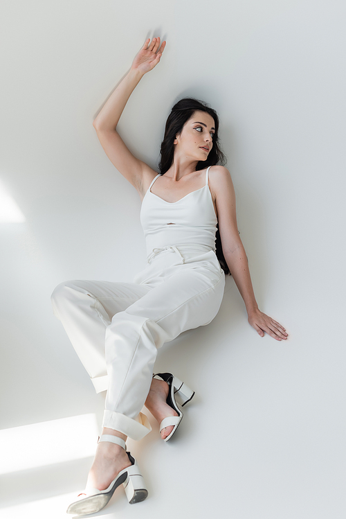 Trendy model in white clothes posing on grey background with sunlight