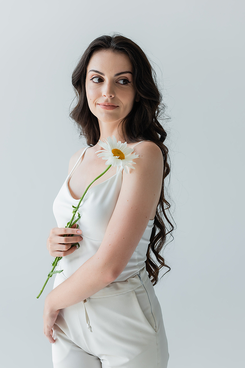 Young woman holding chamomile and looking away isolated on grey