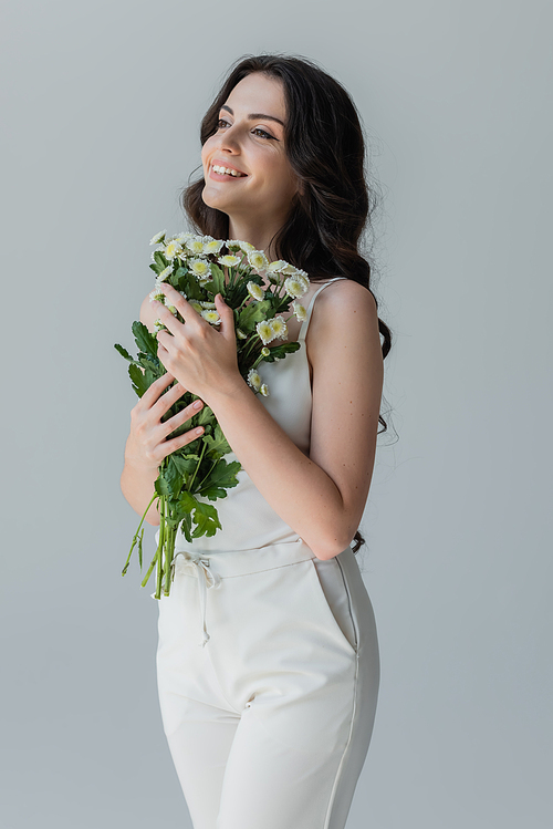 Cheerful woman holding bouquet and looking away isolated on grey