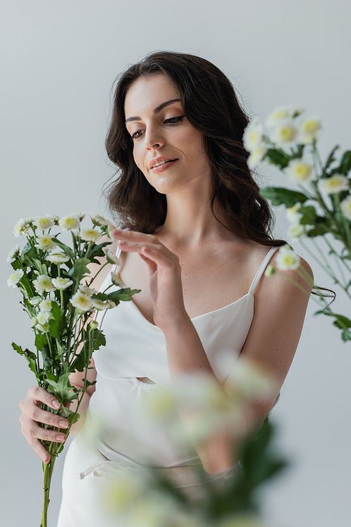 Pretty brunette woman in white top touching flowers isolated on grey