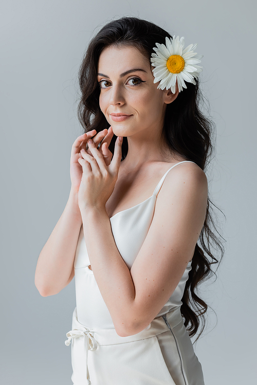 Pretty woman with chamomile in hair looking at camera isolated on grey