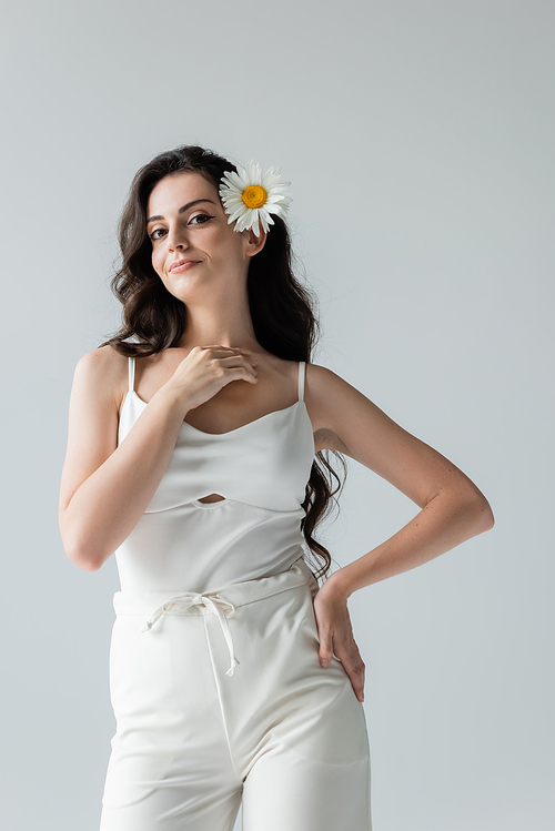 Smiling model in white clothes and chamomile in hair isolated on grey