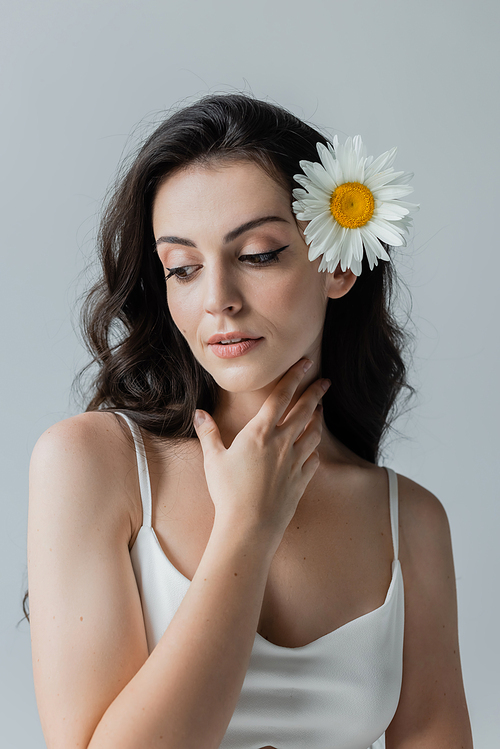 Brunette model in white top with chamomile in hair isolated on grey