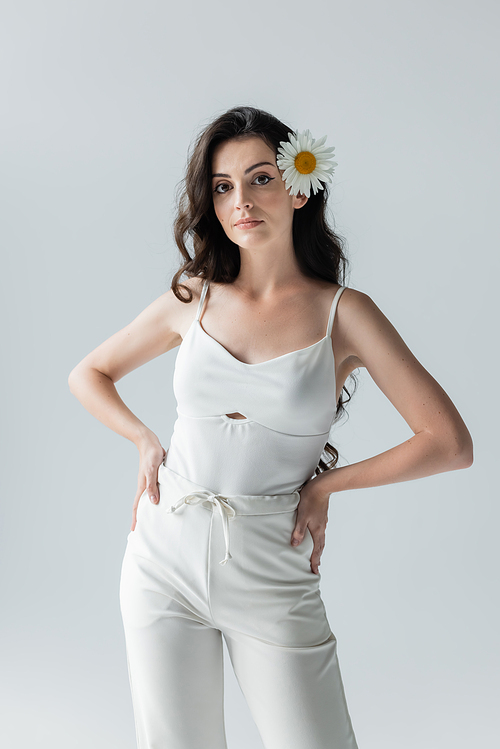Woman in white clothes and with chamomile in hair standing isolated on grey