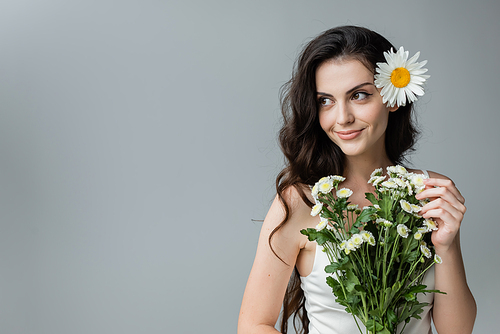 Smiling young woman holding bouquet of chamomiles isolated on grey