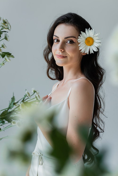 Young woman in white clothes standing near blurred flowers isolated on grey
