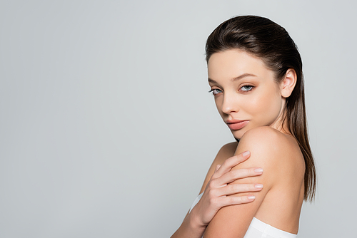 portrait of pretty young woman with bare shoulders and makeup looking at camera isolated on grey