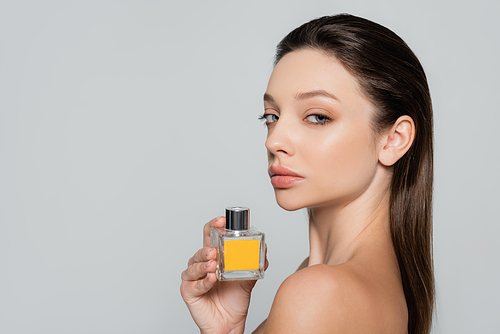 young woman with bare shoulder holding bottle with perfume isolated on grey